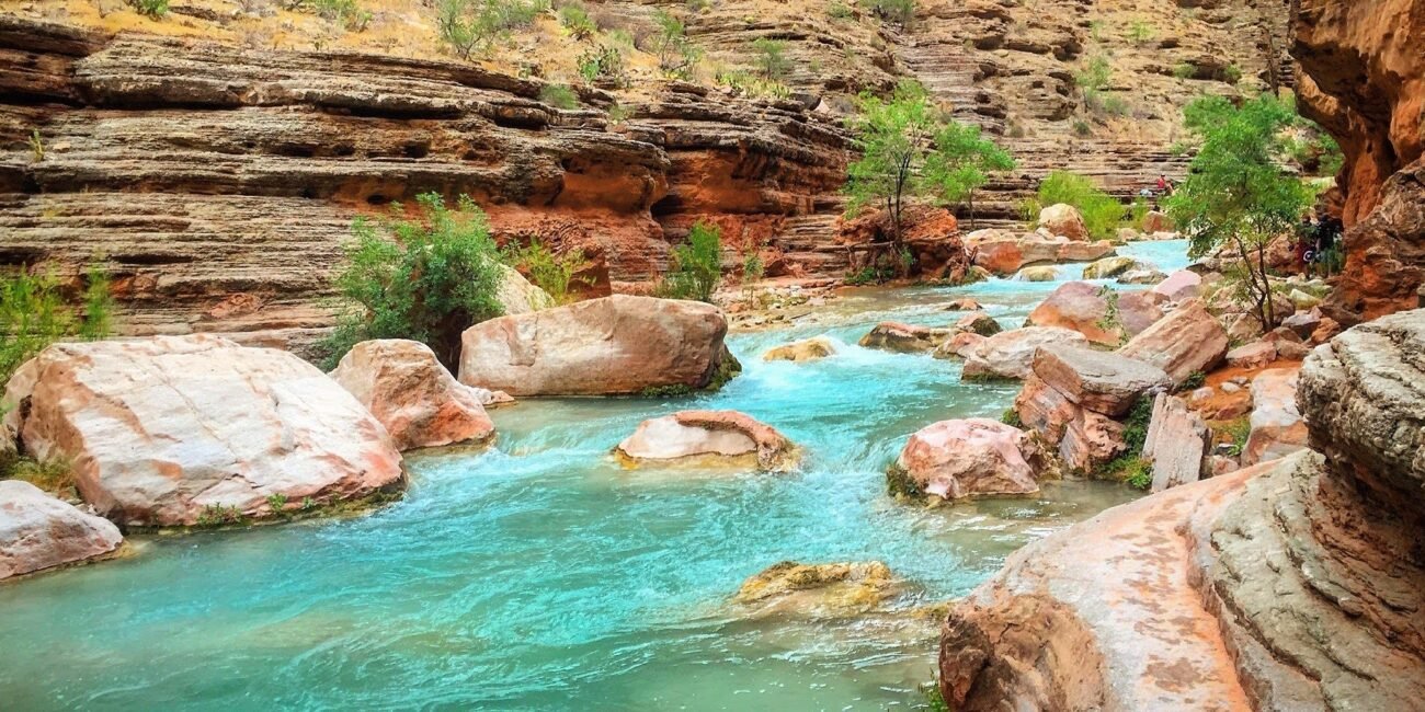 Turquoise Havasu Creek winding between red rock walls and boulders in Havasu Canyon