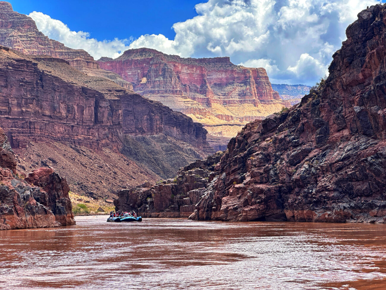 Raft traveling beneath layered cliffs on the Colorado River
