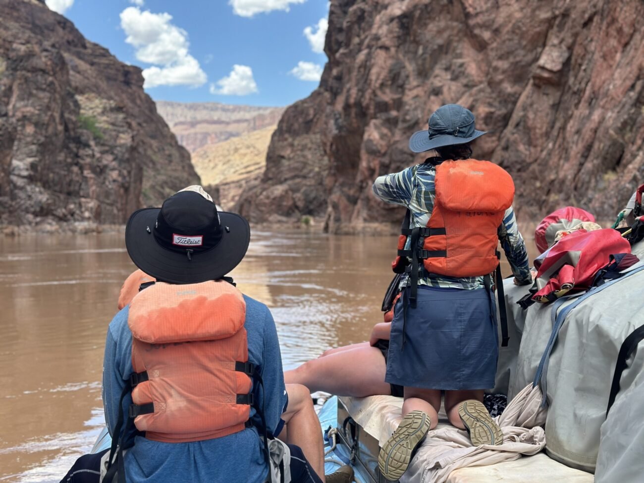 Passengers seated in a raft beneath Grand Canyon walls