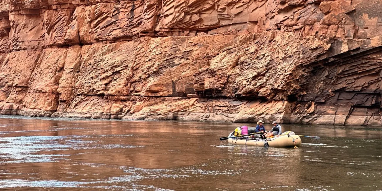 Small raft carrying two passengers beneath red Grand Canyon walls