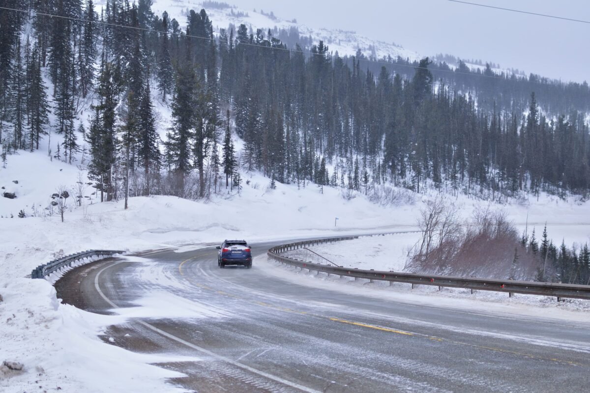 Car driving on a snow-covered pine forest road in winter