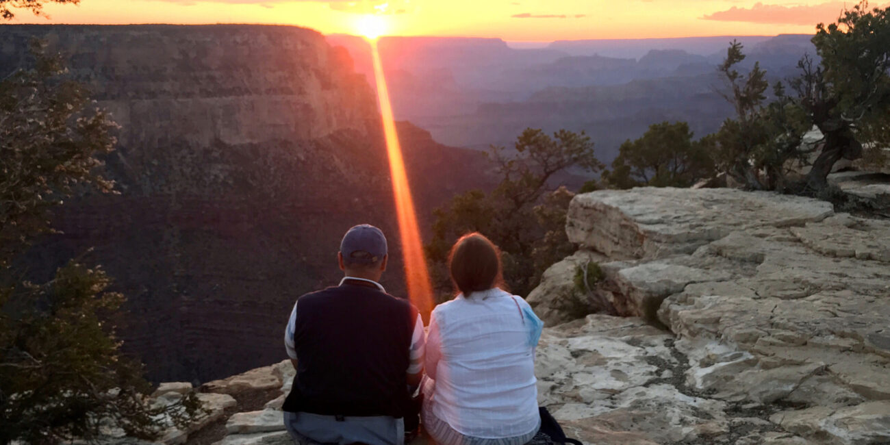 Two visitors seated on a Grand Canyon overlook at sunset